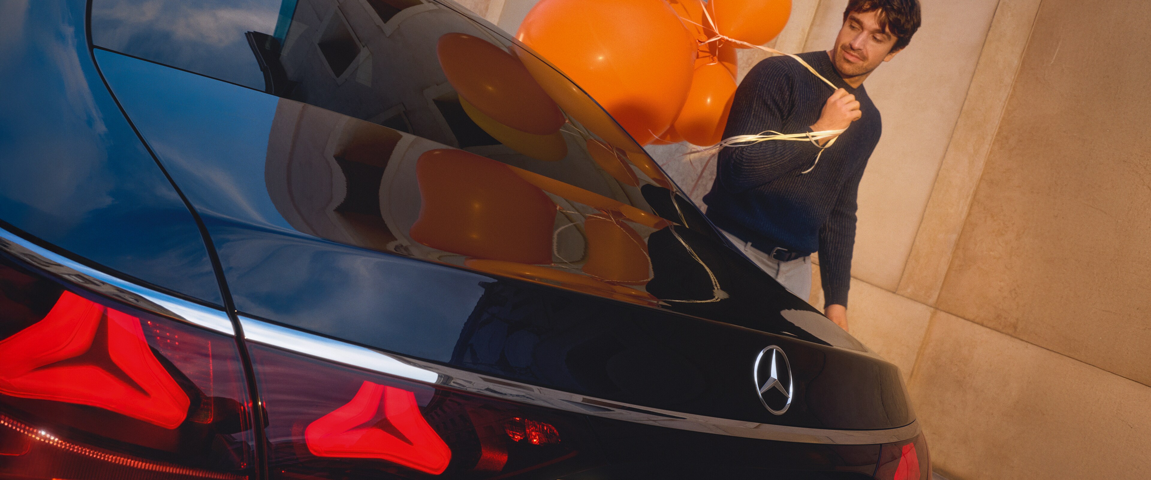 A man with a bunch of balloons walking past a Mercedes-Benz car